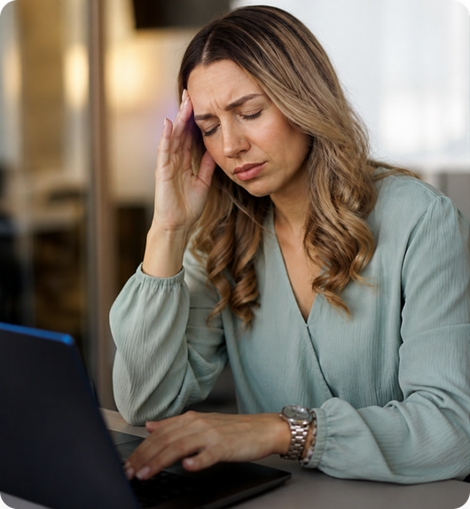 A woman rubbing her temple while working at a laptop